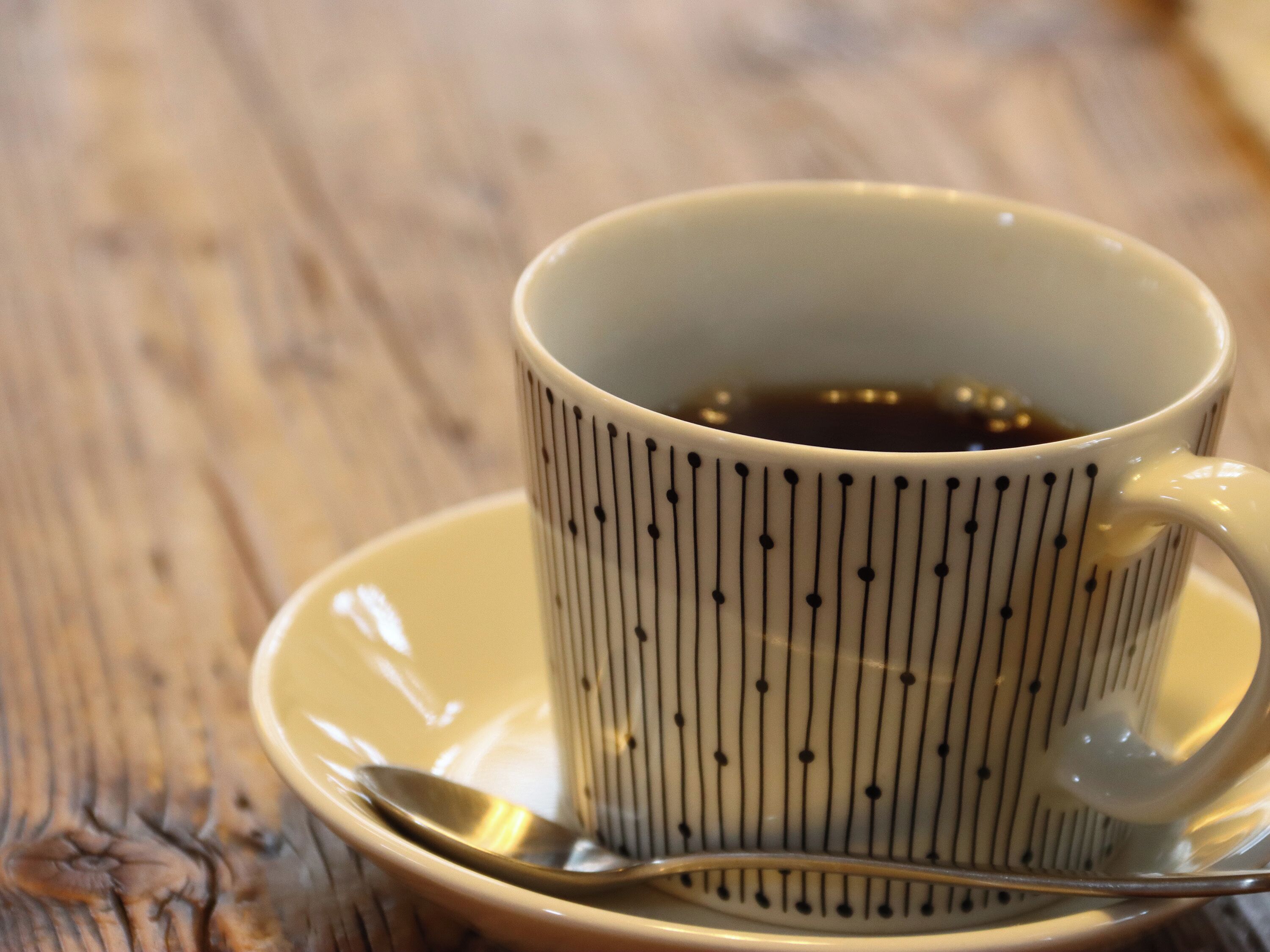 A white ceramic mug with black vertical lines and dots, filled with a dark liquid, likely coffee, on a wooden table.