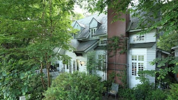 Traditional house surrounded by lush gardens and a paved patio area, featuring a classic gabled roof and brick chimney.