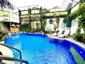 A swimming pool with a tiled edge, surrounded by potted plants and a white chair. - Ngo House 2 Villa (Da Nang)