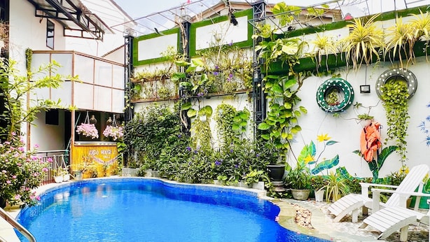 Una piscina con borde de azulejos, rodeada de abundante follaje y plantas.