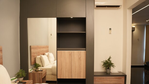 A modern hotel room with a bed, a wooden nightstand, a small table with a plant, a built-in wardrobe, and a potted plant on the nightstand. - B Residence (Beirut)