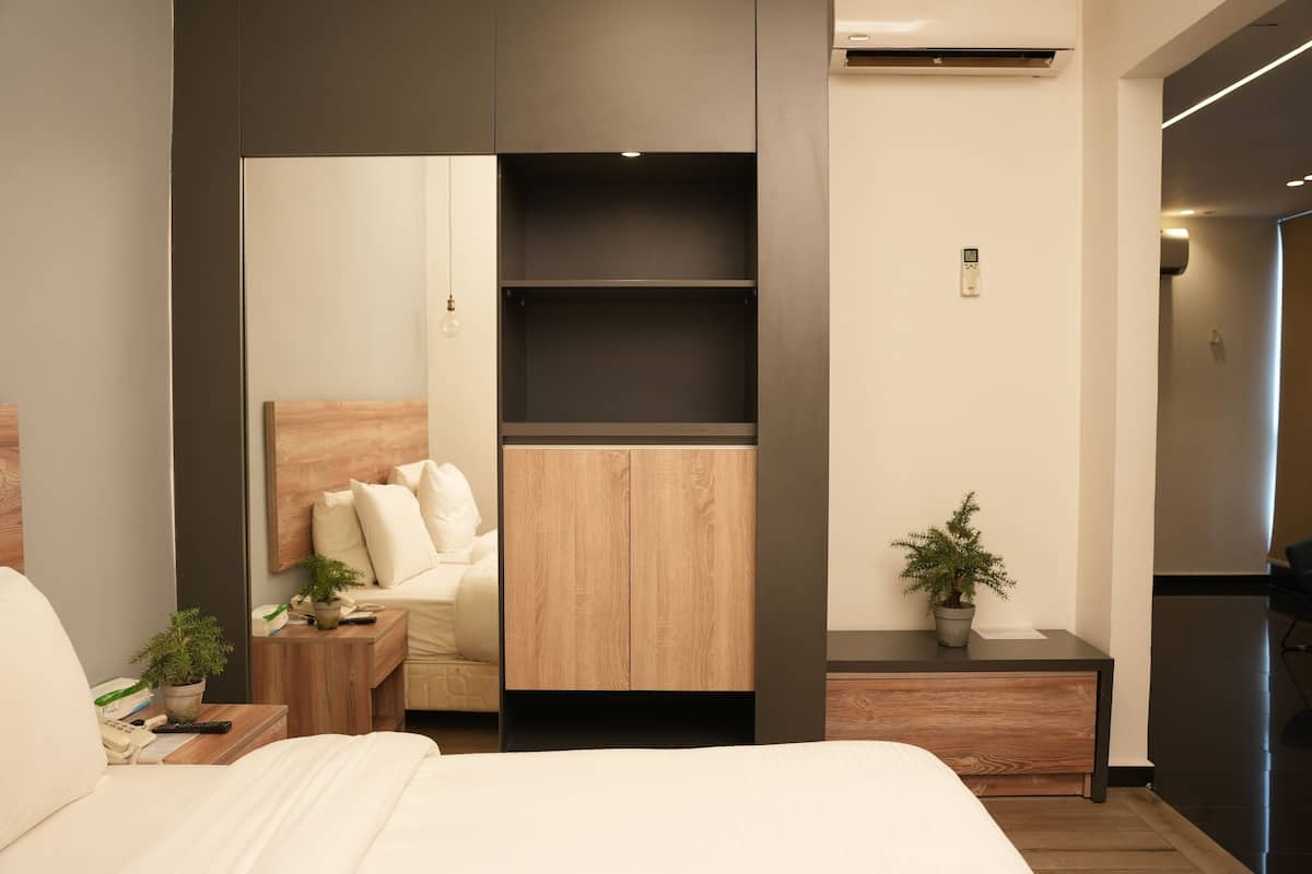 Ein modernes Hotelzimmer mit einem Bett, einem Nachttisch aus Holz, einem kleinen Tisch mit einer Pflanze, einem integrierten Kleiderschrank und einer Topfpflanze auf dem Nachttisch.