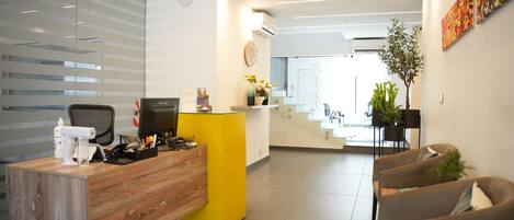 A modern reception area with a wooden desk, a yellow counter, and a seating area with sofas.