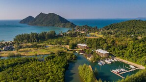 An aerial view of a coastal area with a marina, a large building, and a mountain in the background. - Marina Sands Resort (Ko Chang)