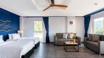 Ein Hotelzimmer mit einem großen Bett, zwei Einzelbetten, einer Couch, einem Couchtisch und einem Deckenventilator.