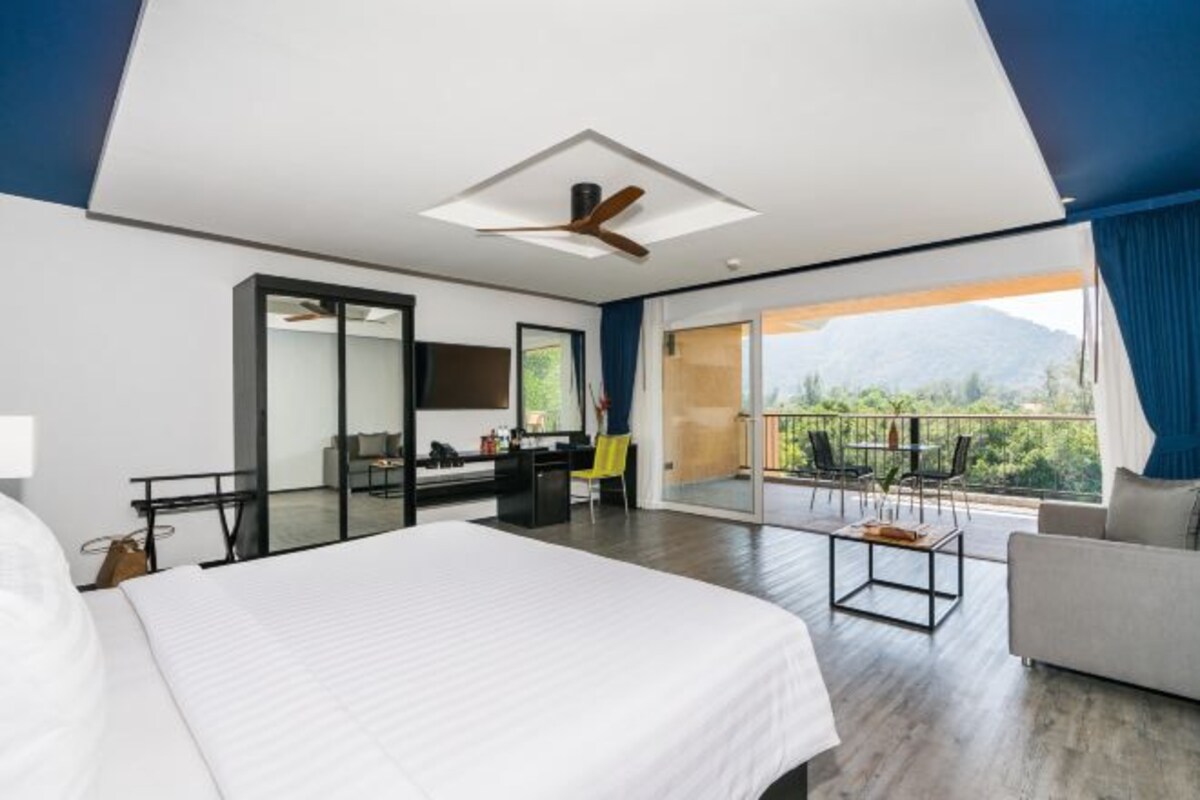 Una habitación de hotel moderna con una cama grande, un escritorio, una silla y un balcón con vistas a las montañas.