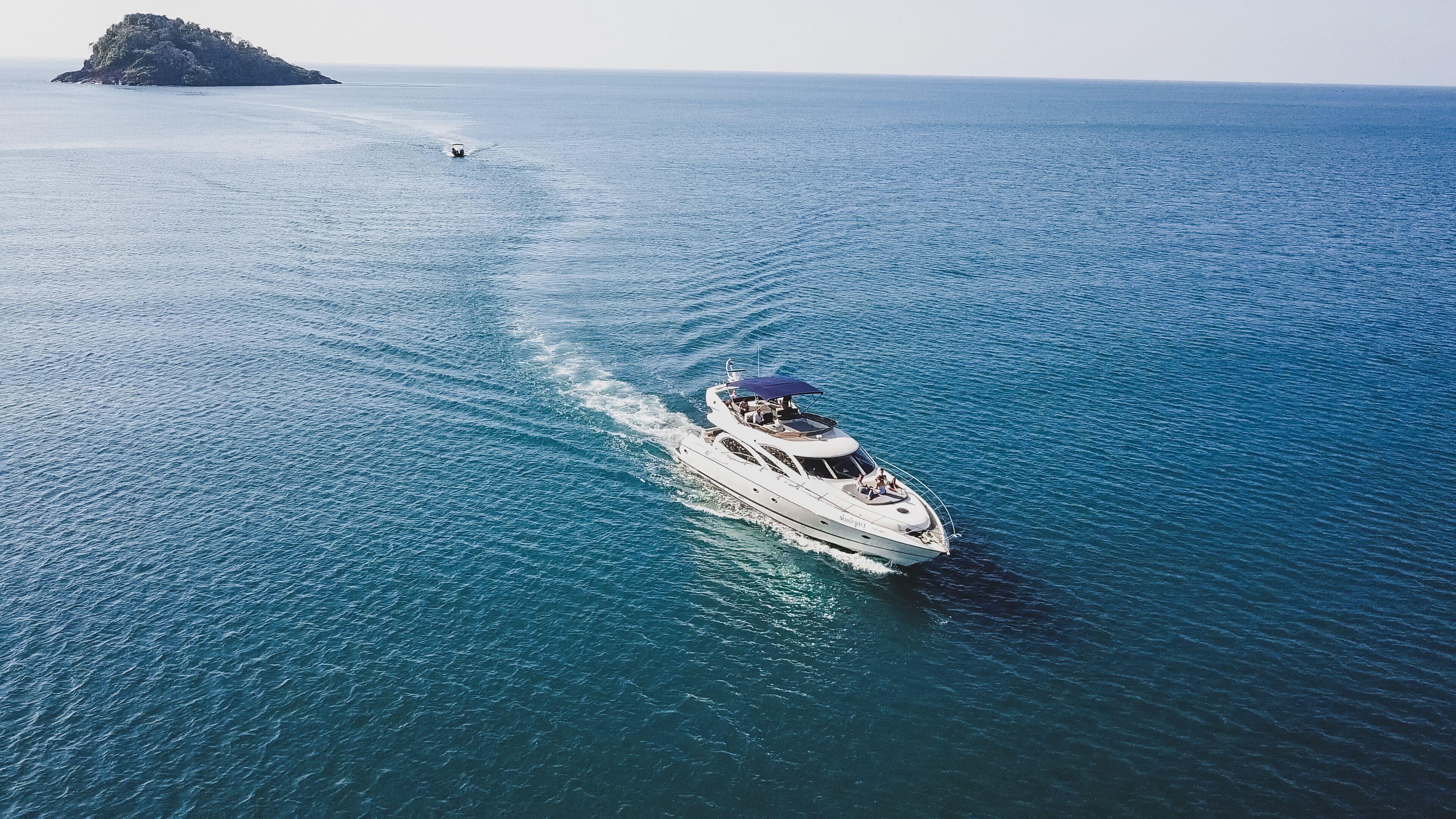 Un yacht navigue sur une mer calme, avec une petite île en arrière-plan.
