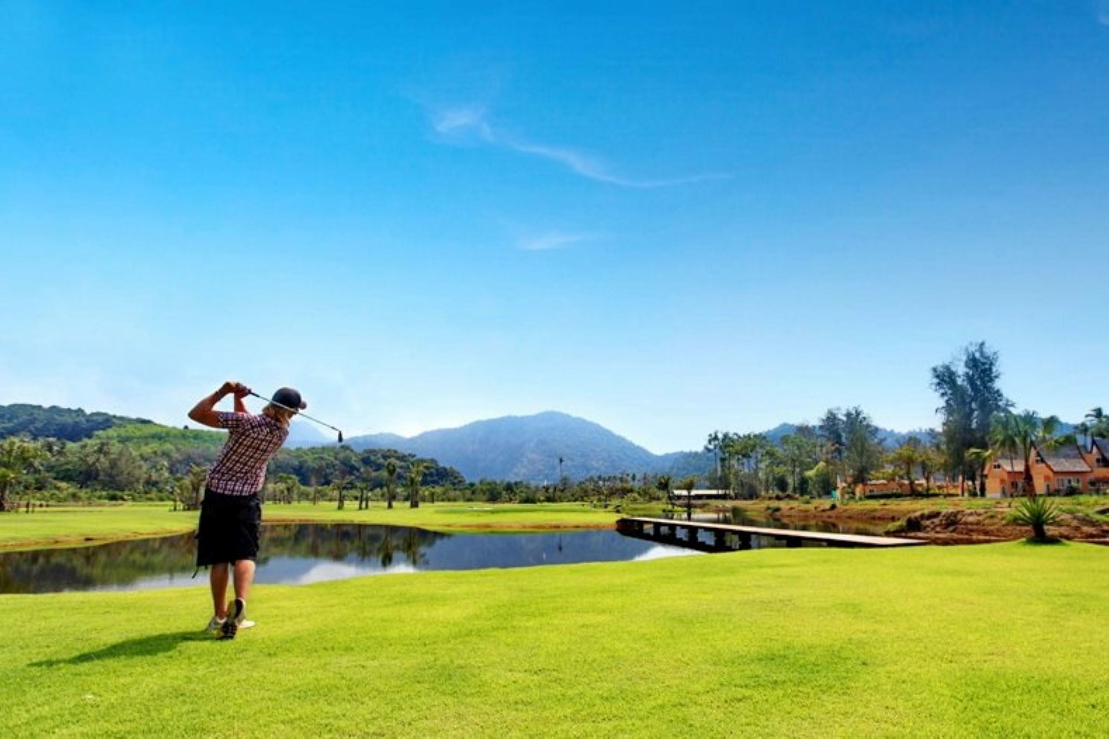 A golf course with a pond, a bridge, and a mountain in the background.