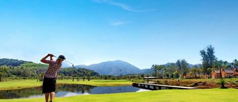 A golf course with a pond, a bridge, and a mountain in the background.