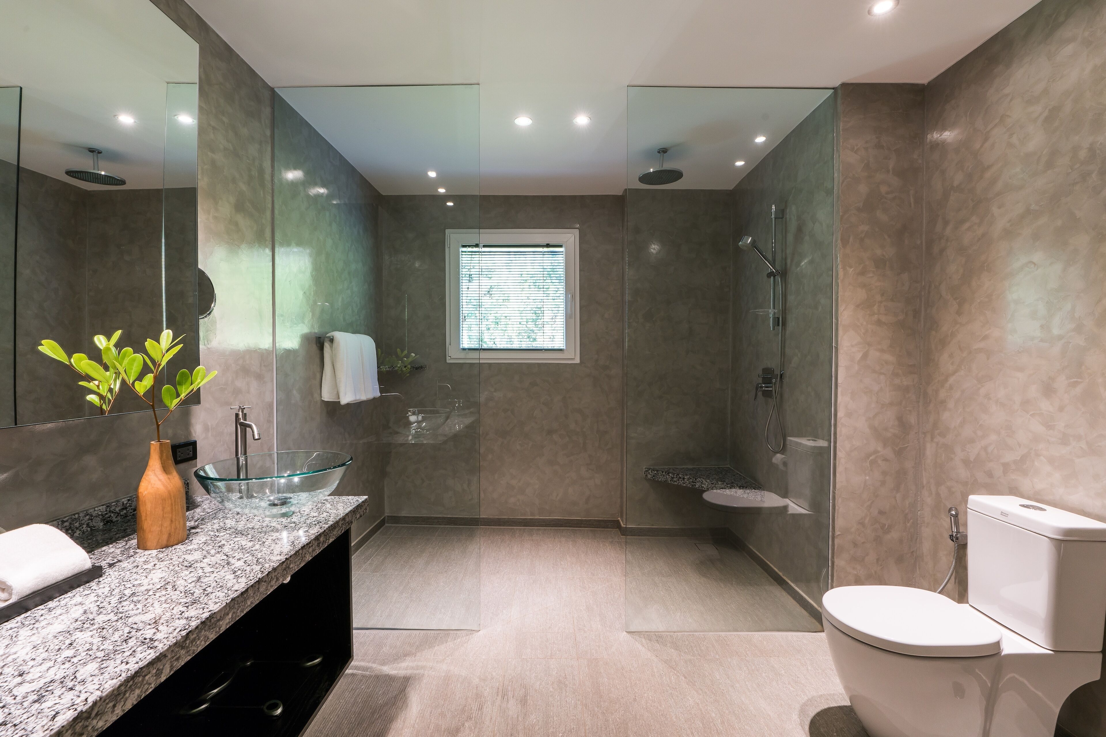 A modern bathroom with a glass bowl sink, a wooden vase, a towel, and a toilet.