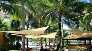 An outdoor seating area with tables and chairs under shade structures, surrounded by palm trees and a view of the sea. - Marina Sands Resort (Ko Chang)