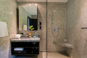 Ein modernes Badezimmer mit einer gläsernen Duschkabine, einem Waschtisch mit Granitplatte, einem großen Spiegel und einer kleinen Pflanze.