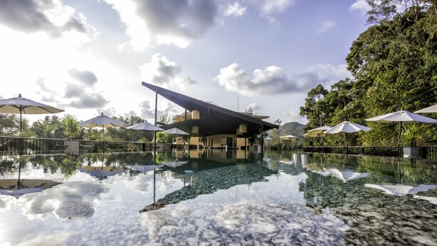 A modern building with a unique roof design, surrounded by a reflective pool and lush greenery. - Marina Sands Resort (Ko Chang)