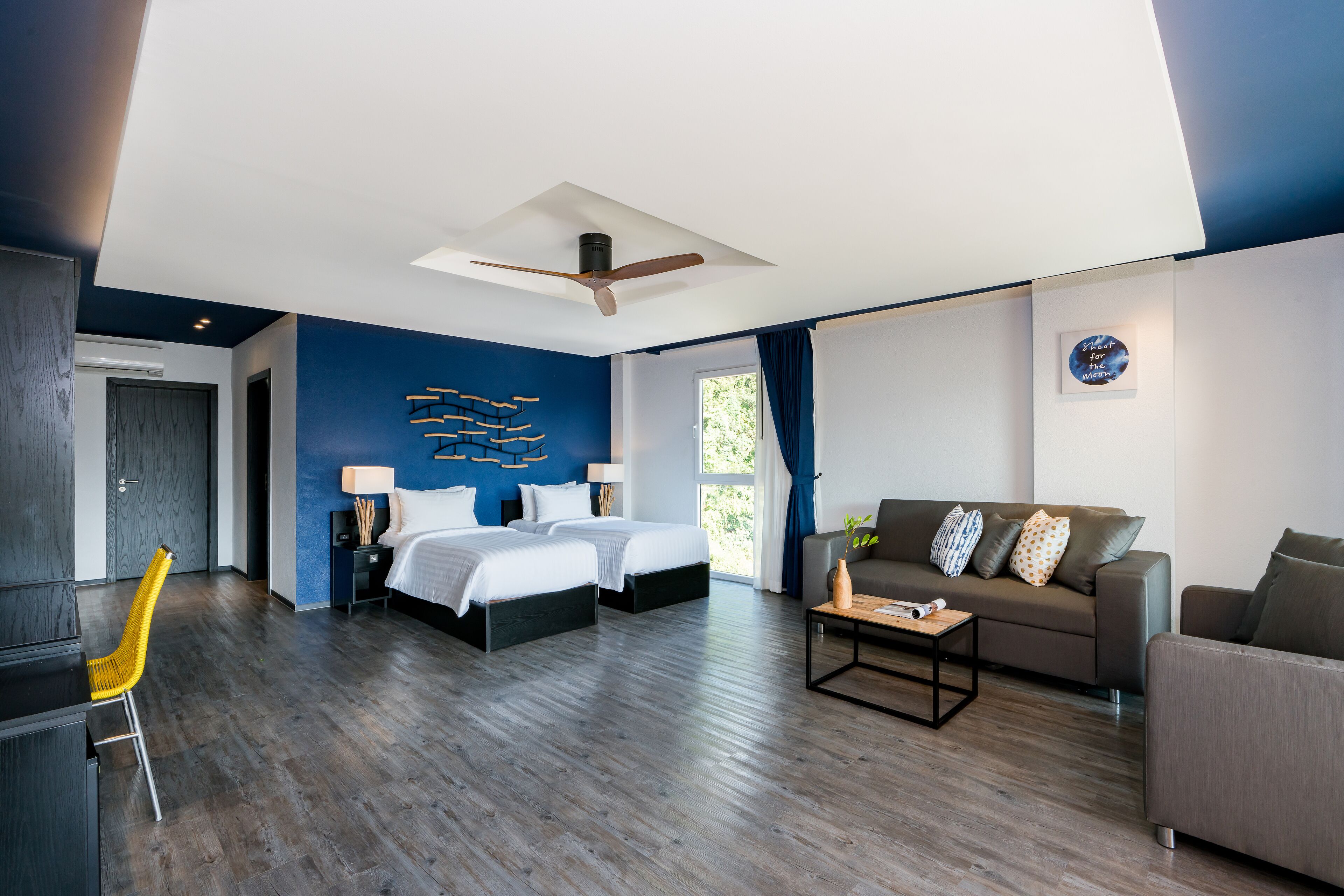 A modern hotel room with a large bed, a sofa, a desk, and a chair.