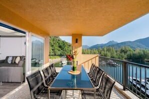 Ein Balkon mit Tisch, Stühlen, einer Couch und Blick auf Berge und Wasser.