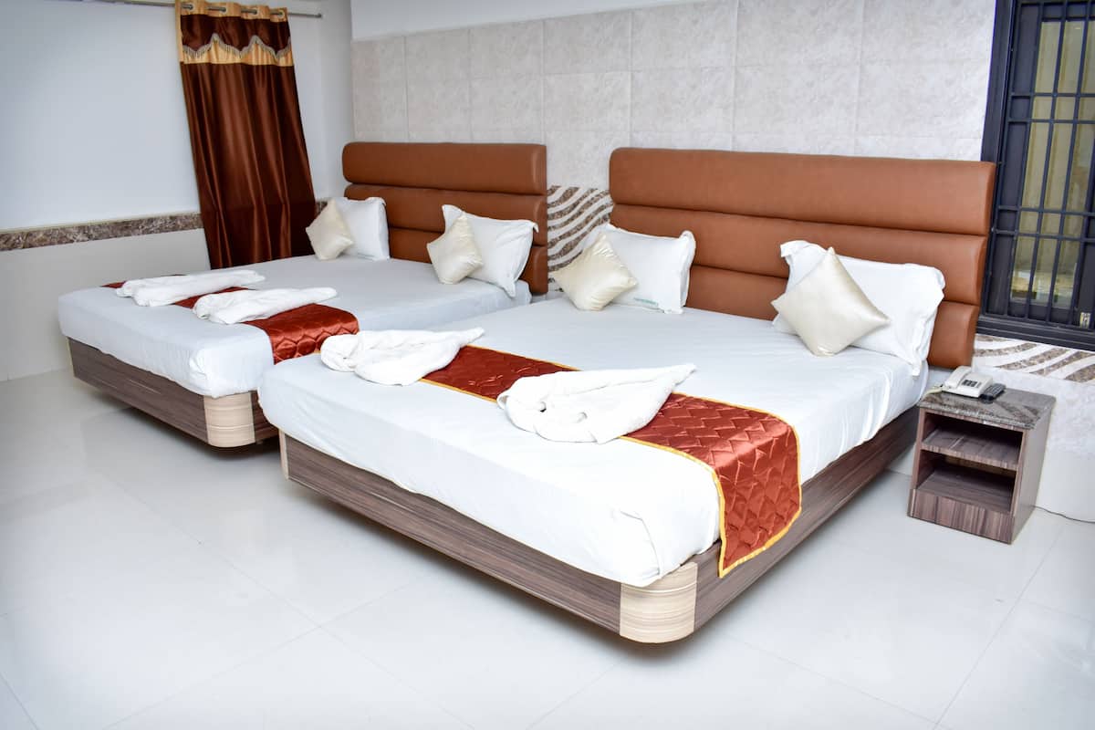 A hotel room with two beds, each with a brown headboard, white bedding, and a red accent. There is a small wooden nightstand with a phone and a remote control.