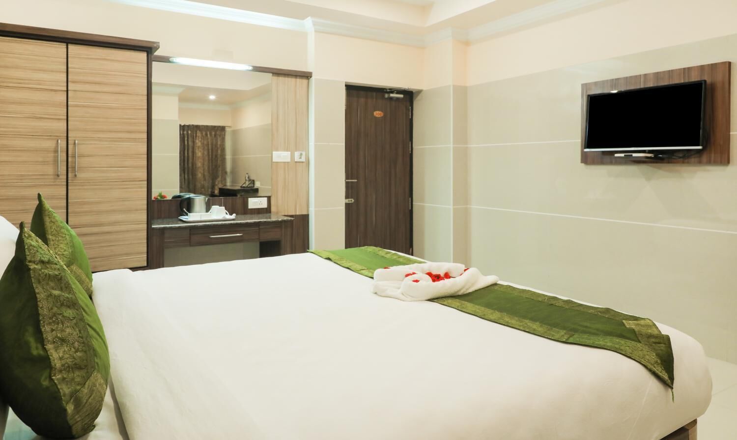 Una habitación de hotel con una cama, un televisor montado en la pared, un armario y un espejo.