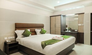 A modern hotel room with a large bed, a nightstand, a dresser, and a mirror. - Sakthi Residency (Kumbakonam)