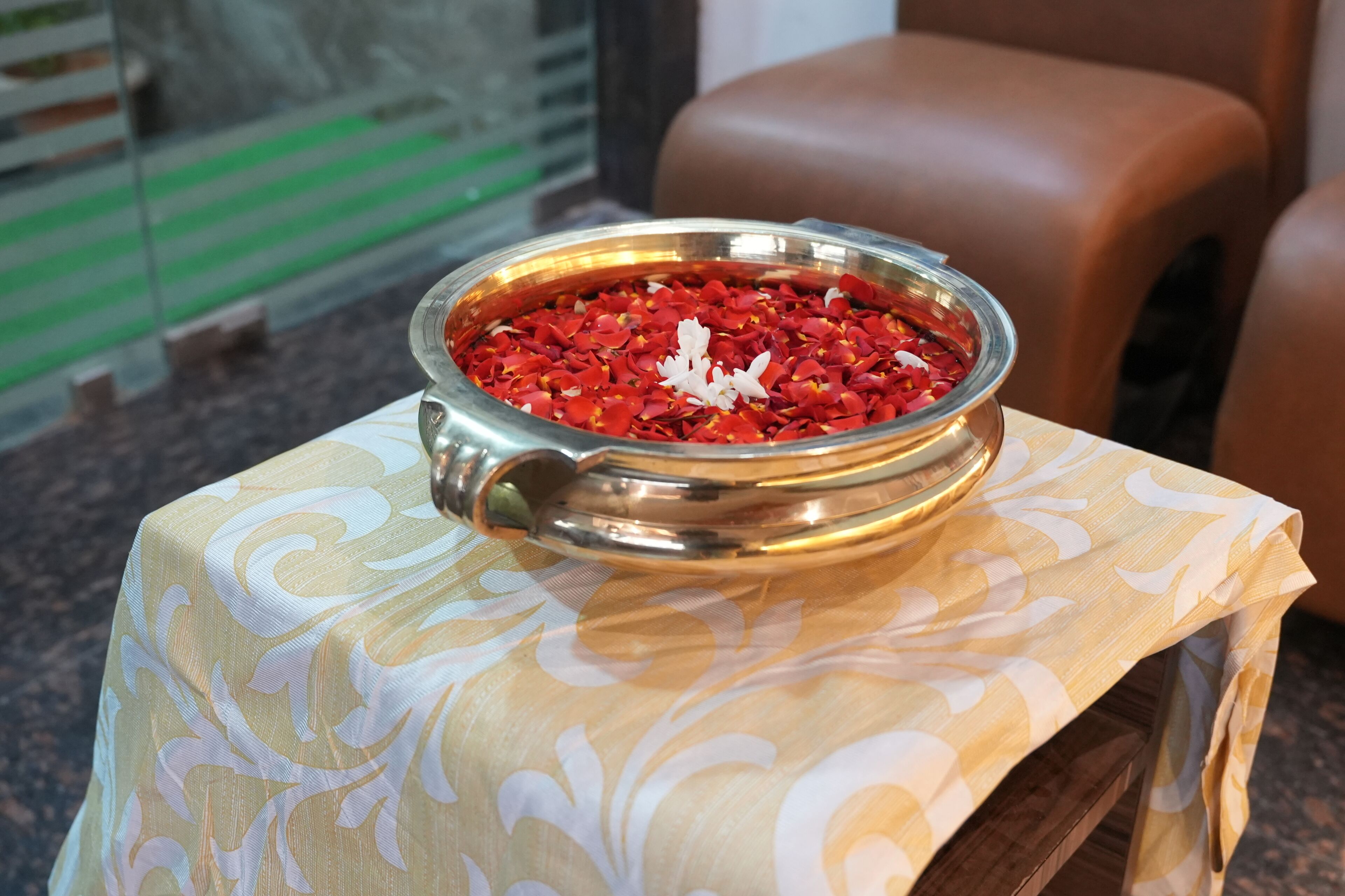 Un tazón metálico lleno de pétalos rojos sobre una mesa con mantel estampado.