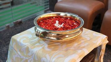 Un tazón metálico lleno de pétalos rojos sobre una mesa con mantel estampado.