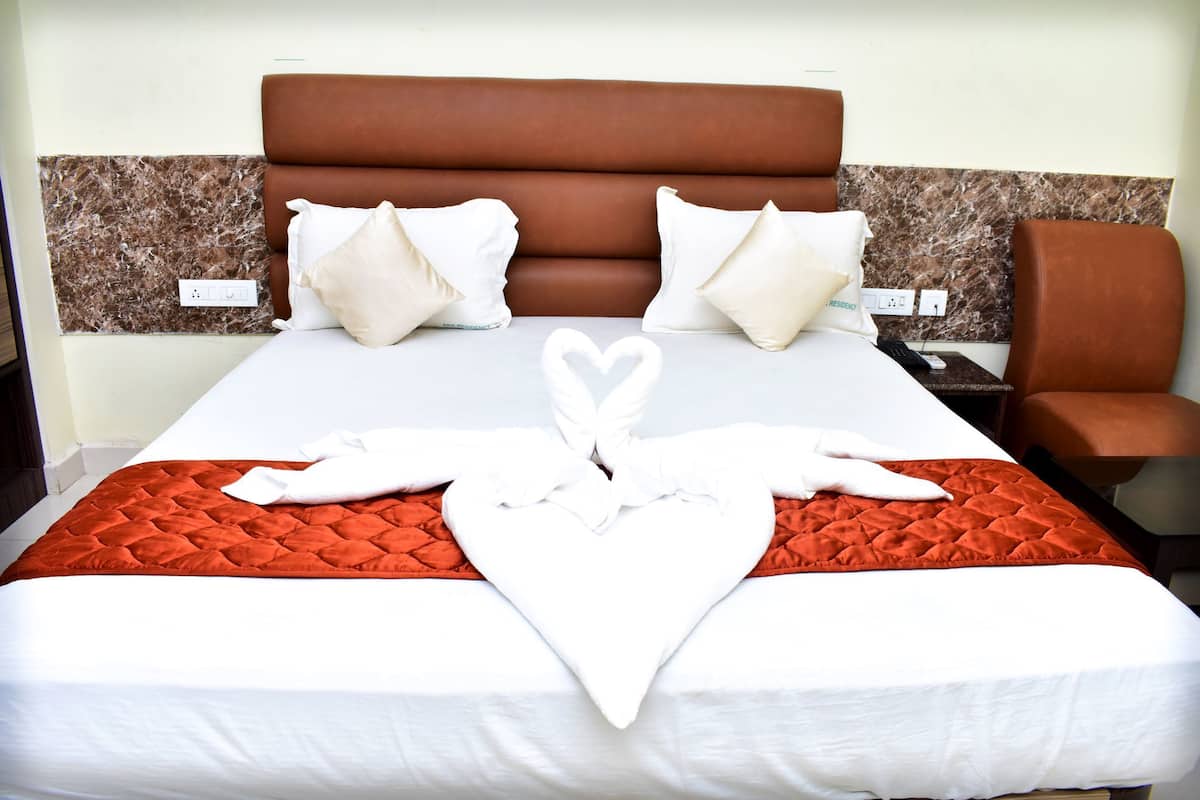 A neatly made bed with a heart-shaped towel arrangement, a brown headboard, and white pillows.