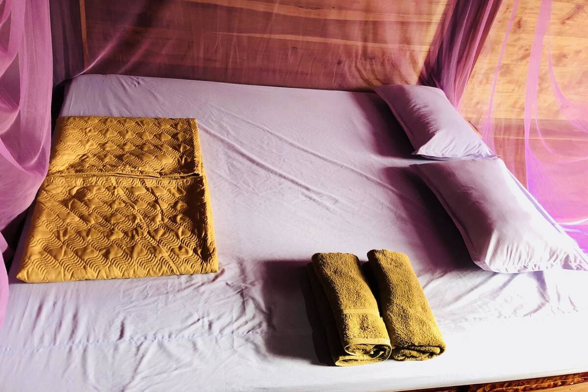 A bed with a white sheet, a yellow quilt, and two rolled towels.