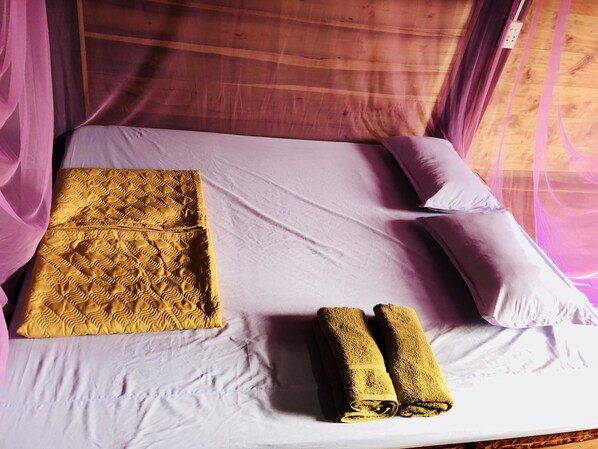 Una cama con sábana blanca, colcha amarilla y dos toallas enrolladas.