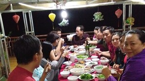 A group of people seated around a table with various dishes, in a covered outdoor area with a metal roof structure. - Hoang Hop Homestay - Hostel (Ba Be)