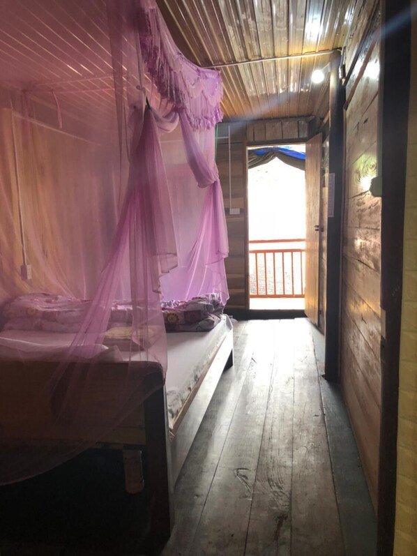 A wooden room with a bed covered by a purple canopy.