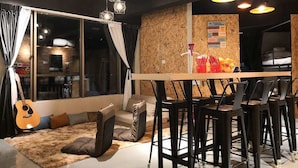 A modern interior with a dining area, a sofa with cushions, a guitar, and a bulletin board with notes. - Homy Seafront Hostel (Kota Kinabalu)