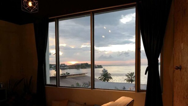 A room with a large window overlooking a body of water, a chair, and a bed. - Homy Seafront Hostel (Kota Kinabalu)