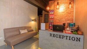 A reception area with a brick wall, a sofa, and a reception desk labeled "RECEPTION". - Homy Seafront Hostel (Kota Kinabalu)