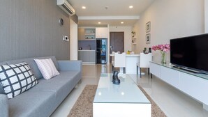 Un salon moderne avec un canapé gris, une table basse en verre et un téléviseur à écran plat posé sur un meuble blanc.
