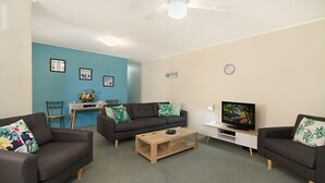 A modern living room with two dark sofas, a wooden coffee table, a TV, and a desk with a chair. - Kingston Court Unit 11 Right on the beach in Rainbow Bay Coolangatta (Coolangatta)