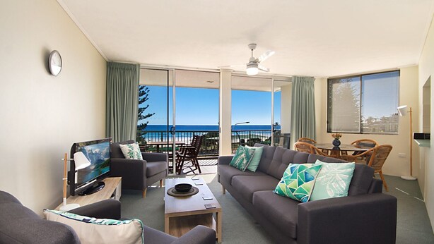 A living room with a sofa, coffee table, and TV, overlooking a balcony with a view of the ocean. - Kingston Court Unit 11 Right on the beach in Rainbow Bay Coolangatta (Coolangatta)