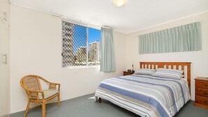 A bedroom with a bed, a chair, a nightstand, and a window with a view of buildings. - Kingston Court Unit 11 Right on the beach in Rainbow Bay Coolangatta (Coolangatta)