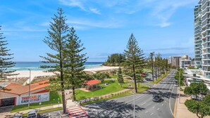 Vista costera con playa, carretera y un edificio con un cartel que dice 'TAKE CARE OF EACH OTHER'.