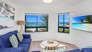 Una habitación con sofá azul, una mesita redonda y dos amplias ventanas con vistas al océano.