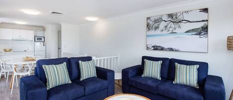A modern living room with two dark blue sofas, a white coffee table, and a large painting of a snowy landscape.