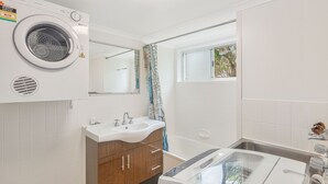 Une salle de bain moderne équipée d’un lave-linge intégré, d’un lavabo avec un miroir et d’une fenêtre donnant sur des arbres.