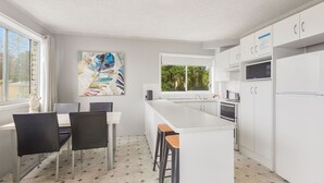 Une cuisine moderne avec des meubles blancs, un grand îlot central, des tabourets de bar noirs et un tableau accroché au mur.