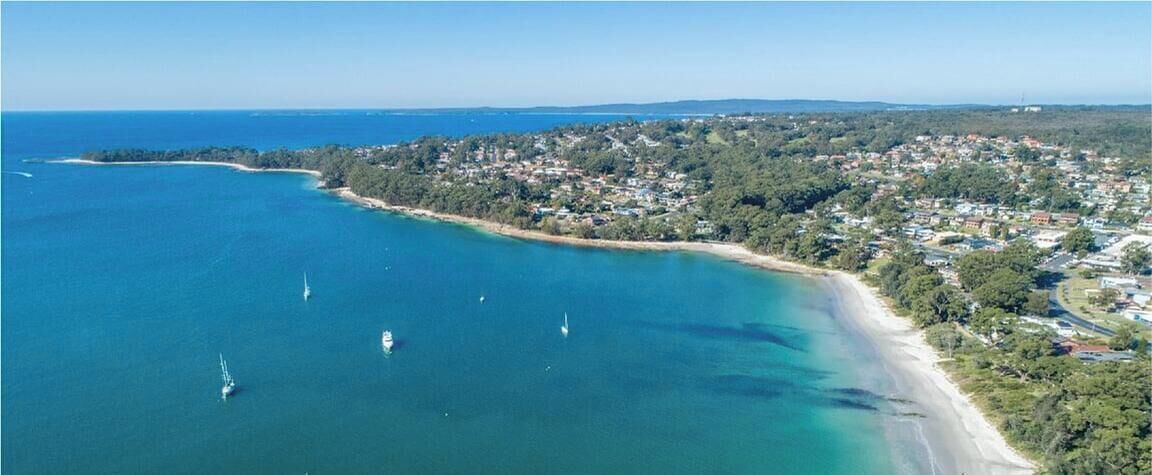Vue aérienne d’une ville côtière avec une plage, des eaux cristallines et plusieurs bateaux.