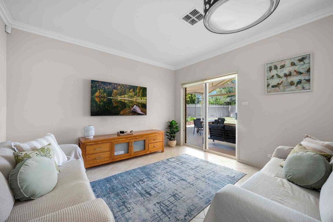 A living room with a sofa, a wooden cabinet, a painting, and a view through a glass door.
