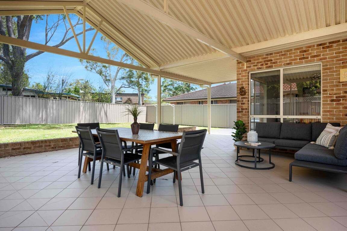 A covered patio with a brick wall, a dining table with chairs, and a sofa.