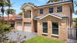 Une maison à deux étages, construite en briques, avec un garage, un balcon et une pelouse bien entretenue.