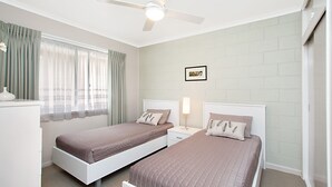 A bedroom with two beds, a ceiling fan, a bedside table with a lamp, and a framed picture on the wall.