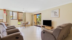 Ein Wohnzimmer mit einer Sofagarnitur, einem Fernseher und einem Essbereich mit Tisch und Stühlen.