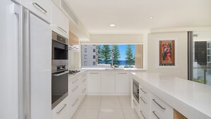 A modern kitchen with white cabinetry, stainless steel appliances, and a view of trees and a building through a window.