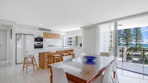 Une cuisine moderne avec des meubles blancs, un îlot central et un coin repas comprenant une table et des chaises en verre.