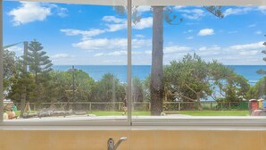 Vista desde una ventana sobre una playa con árboles y cielo despejado.